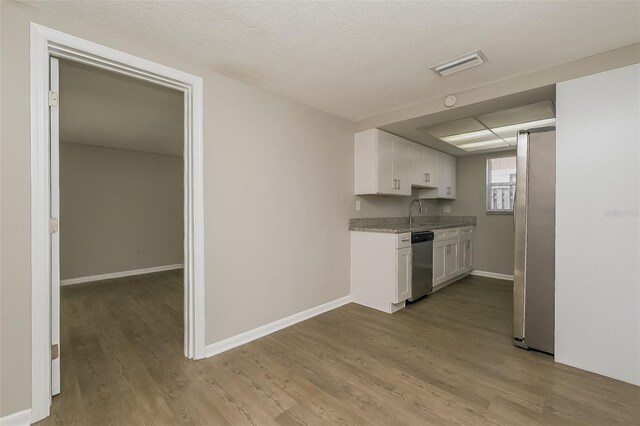 kitchen featuring stainless steel appliances, white cabinets, light stone countertops, light hardwood / wood-style flooring, and a textured ceiling