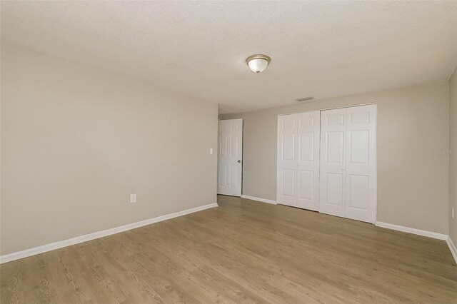 unfurnished bedroom featuring a closet, a textured ceiling, and light wood-type flooring