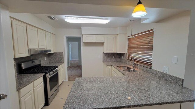 kitchen featuring stainless steel gas stove, hanging light fixtures, sink, light colored carpet, and backsplash