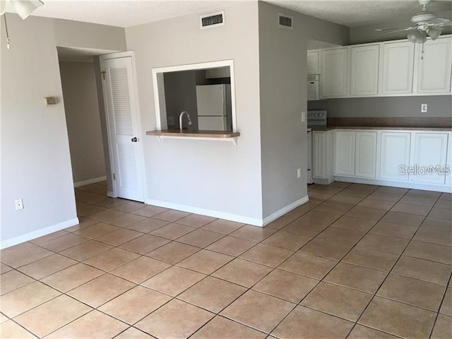 interior space with light tile patterned floors, white cabinets, ceiling fan, white refrigerator, and stove