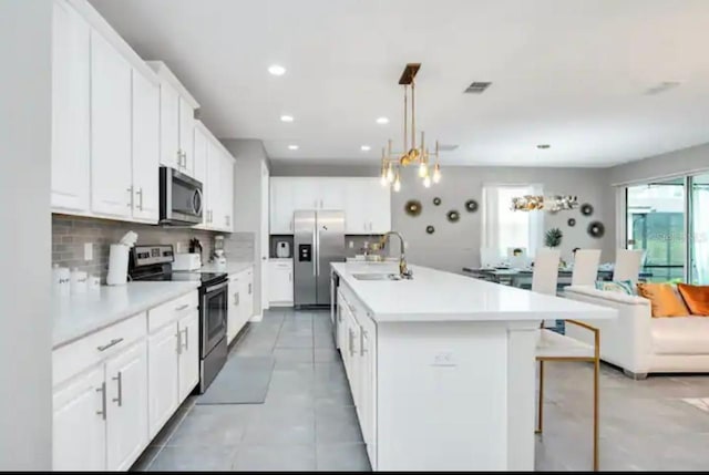 kitchen with appliances with stainless steel finishes, a center island with sink, sink, light tile patterned floors, and white cabinetry