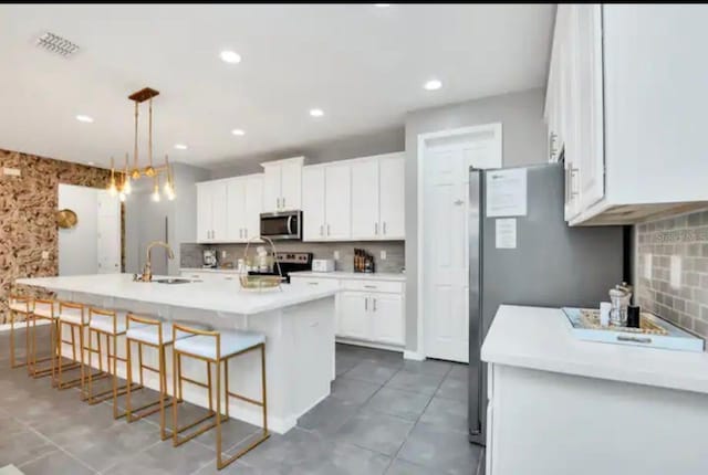 kitchen with appliances with stainless steel finishes, sink, light tile patterned floors, a kitchen island with sink, and white cabinetry