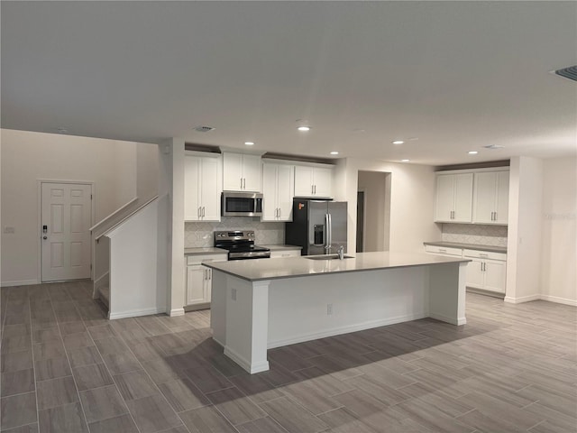 kitchen with appliances with stainless steel finishes, a breakfast bar area, white cabinets, backsplash, and a center island with sink