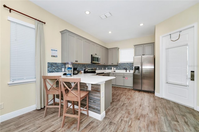 kitchen with kitchen peninsula, gray cabinetry, stainless steel appliances, and a breakfast bar area