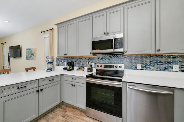 kitchen with light wood-type flooring, backsplash, gray cabinetry, and appliances with stainless steel finishes