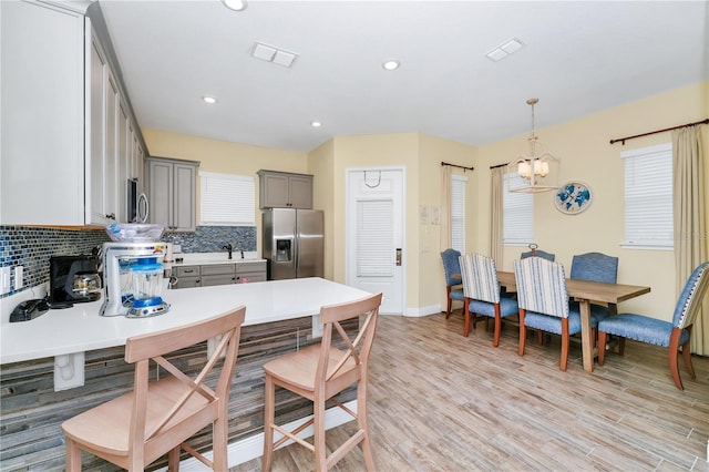 kitchen with decorative light fixtures, stainless steel appliances, tasteful backsplash, gray cabinets, and light hardwood / wood-style flooring