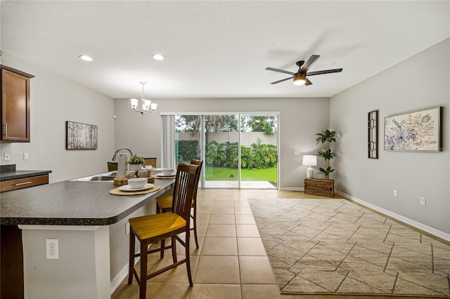 dining area with light tile patterned flooring, ceiling fan with notable chandelier, sink, and a textured ceiling