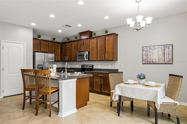 kitchen featuring pendant lighting, sink, stainless steel appliances, an island with sink, and dark stone counters