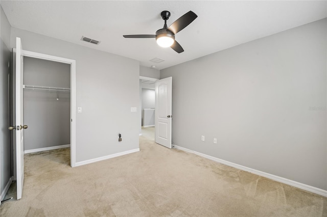 unfurnished bedroom featuring ceiling fan, light colored carpet, a closet, and a walk in closet