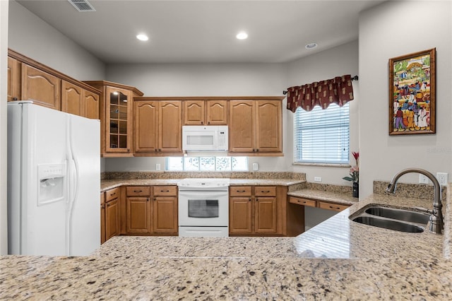 kitchen featuring light stone counters, white appliances, and sink