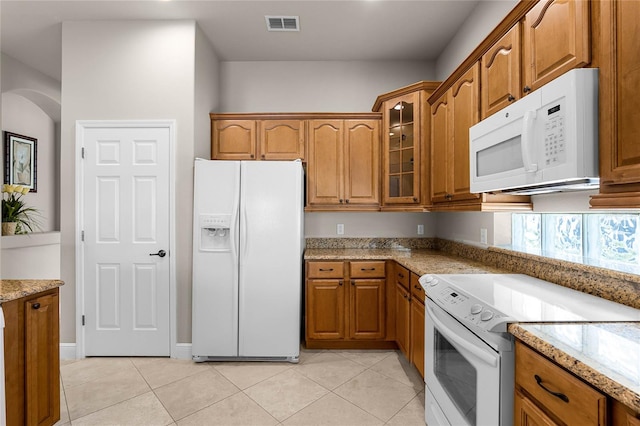 kitchen featuring light tile patterned flooring, light stone counters, and white appliances