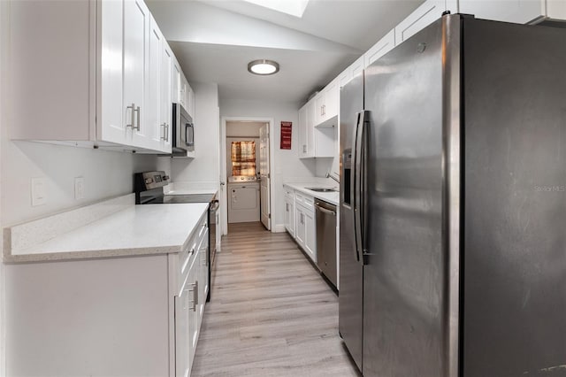 kitchen featuring sink, appliances with stainless steel finishes, lofted ceiling with skylight, light hardwood / wood-style floors, and white cabinets