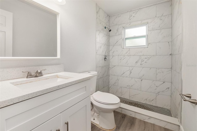 bathroom featuring hardwood / wood-style flooring, vanity, a tile shower, and toilet