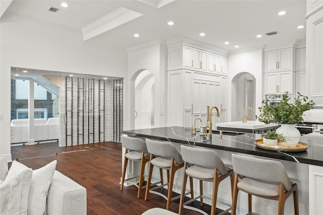 kitchen featuring dark hardwood / wood-style flooring, ornamental molding, sink, white cabinetry, and a breakfast bar area