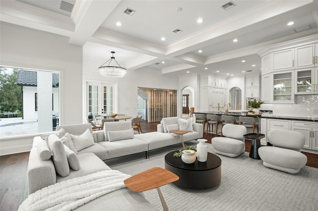 living room featuring coffered ceiling, an inviting chandelier, beamed ceiling, crown molding, and wood-type flooring