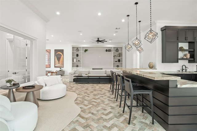 kitchen featuring light stone countertops, a breakfast bar, built in shelves, ceiling fan, and decorative light fixtures