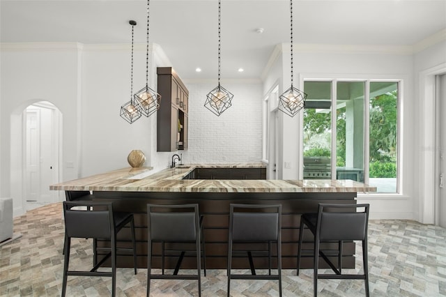 kitchen featuring sink, kitchen peninsula, crown molding, pendant lighting, and a breakfast bar area