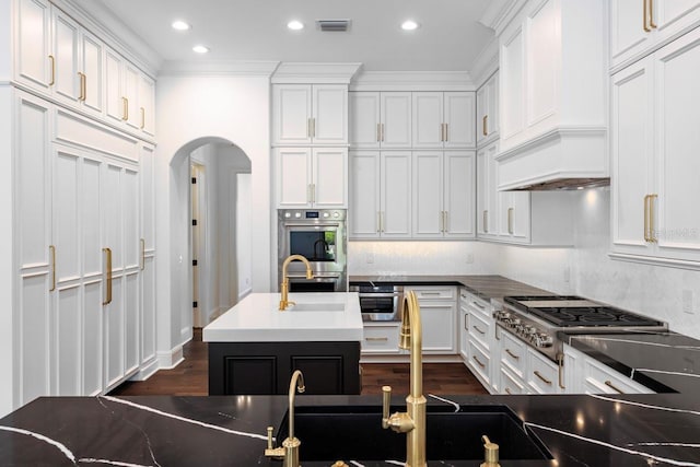 kitchen with sink, stainless steel appliances, crown molding, a center island with sink, and white cabinets