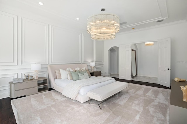 bedroom with a tray ceiling, crown molding, wood-type flooring, and a notable chandelier