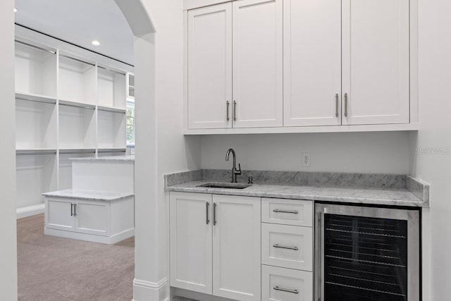 bar with light stone countertops, light colored carpet, beverage cooler, sink, and white cabinetry