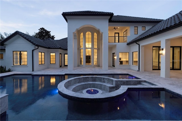 back house at dusk featuring a patio area, ceiling fan, and a swimming pool with hot tub