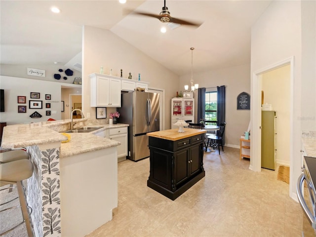 kitchen with stainless steel refrigerator, sink, white cabinets, hanging light fixtures, and kitchen peninsula