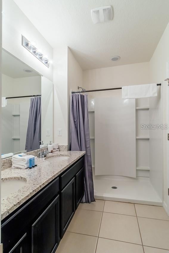 bathroom with a textured ceiling, tile patterned flooring, curtained shower, and vanity