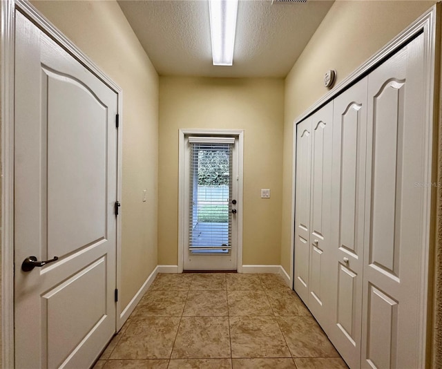 doorway to outside with a textured ceiling and light tile patterned flooring