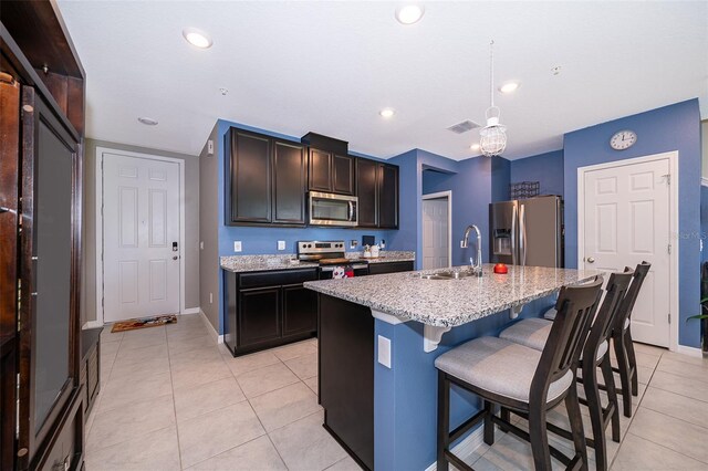 kitchen with light tile patterned flooring, sink, a kitchen bar, appliances with stainless steel finishes, and a kitchen island with sink