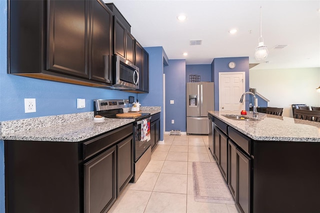 kitchen featuring sink, light stone countertops, appliances with stainless steel finishes, light tile patterned floors, and a kitchen island with sink