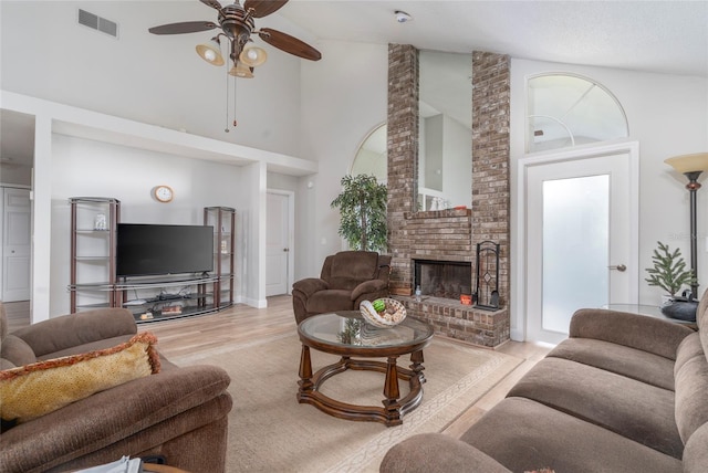 living room with light hardwood / wood-style flooring, a brick fireplace, high vaulted ceiling, brick wall, and ceiling fan