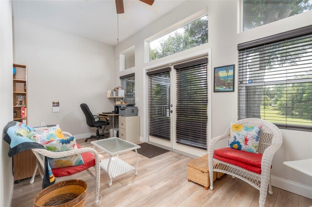 living area with a towering ceiling, light hardwood / wood-style flooring, and ceiling fan