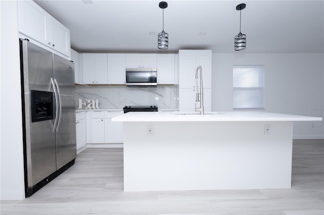 kitchen with white cabinets, backsplash, a kitchen island with sink, appliances with stainless steel finishes, and decorative light fixtures