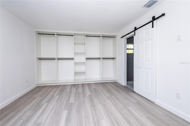 unfurnished bedroom with light wood-type flooring, a closet, and a barn door