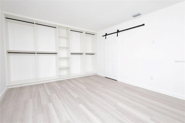 unfurnished bedroom with a barn door and light wood-type flooring