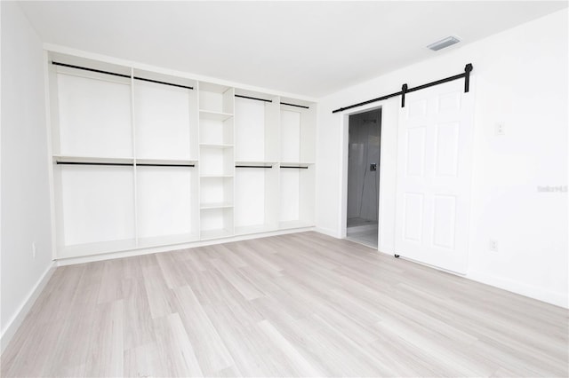 unfurnished bedroom with light wood-type flooring and a barn door