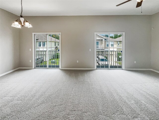 carpeted empty room featuring plenty of natural light and ceiling fan with notable chandelier