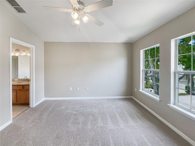 unfurnished bedroom featuring light carpet, multiple windows, and ensuite bathroom