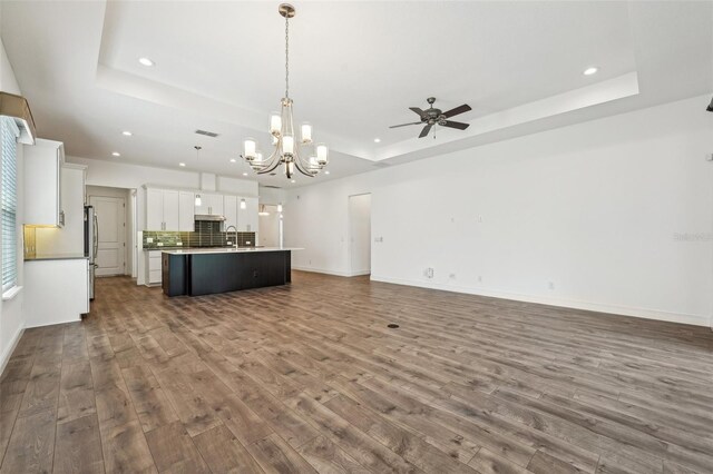 unfurnished living room featuring ceiling fan with notable chandelier, sink, hardwood / wood-style flooring, and a raised ceiling