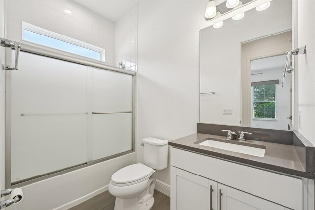 full bathroom featuring hardwood / wood-style flooring, enclosed tub / shower combo, vanity, and toilet