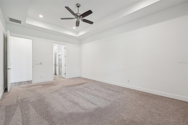 carpeted empty room featuring ceiling fan and a raised ceiling