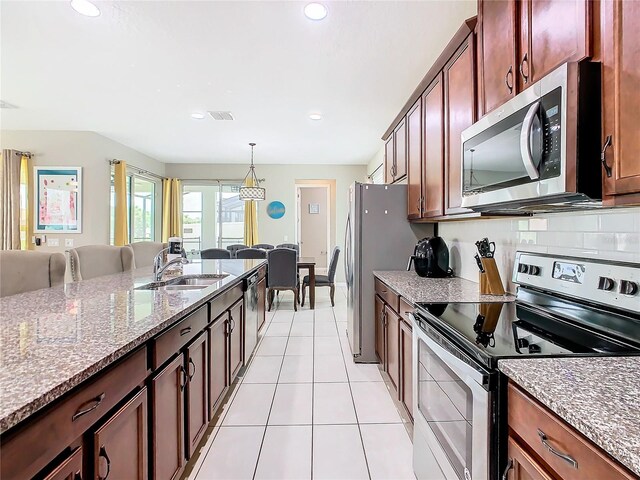 kitchen with pendant lighting, sink, decorative backsplash, light tile patterned floors, and stainless steel appliances