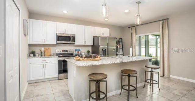 kitchen featuring appliances with stainless steel finishes, light stone countertops, a kitchen island with sink, and light tile patterned floors