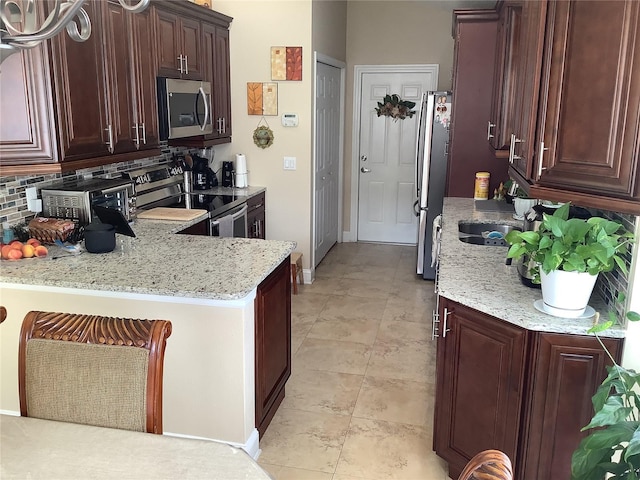 kitchen with sink, appliances with stainless steel finishes, light stone countertops, decorative backsplash, and kitchen peninsula