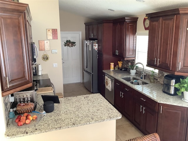 kitchen with sink, appliances with stainless steel finishes, backsplash, light stone counters, and vaulted ceiling