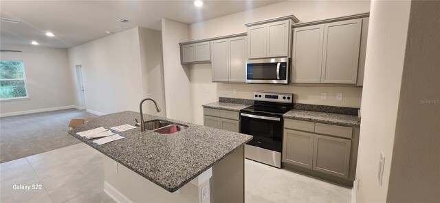 kitchen with light carpet, a center island with sink, gray cabinetry, and appliances with stainless steel finishes