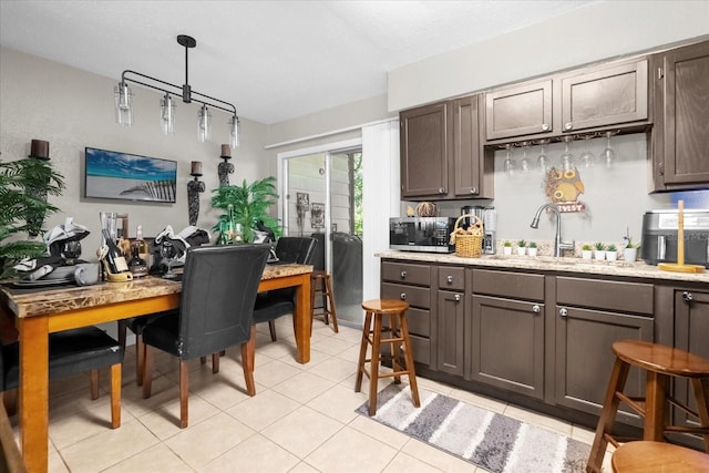 kitchen with dark brown cabinetry, sink, decorative light fixtures, and light tile patterned floors