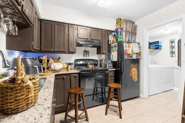 kitchen featuring light tile patterned floors, light stone counters, washing machine and clothes dryer, black appliances, and dark brown cabinetry