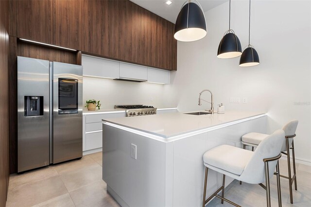 kitchen featuring decorative light fixtures, a kitchen bar, stainless steel appliances, sink, and white cabinetry