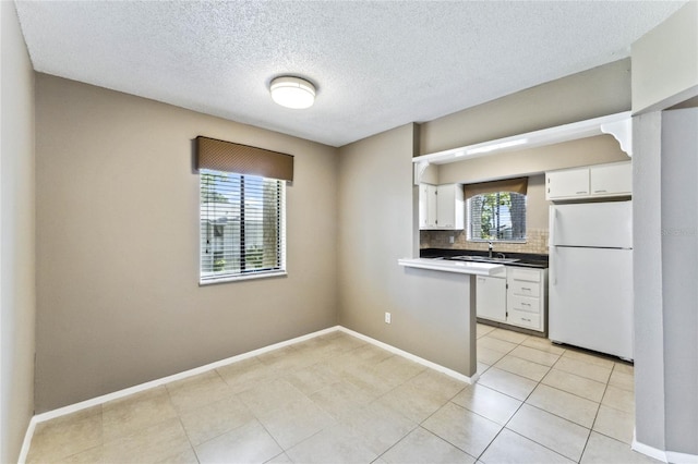 kitchen with white appliances, sink, kitchen peninsula, backsplash, and white cabinets